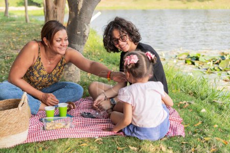 Ein herzlicher Moment mit einer Familie bei einem Picknick am See an einem sonnigen Tag.