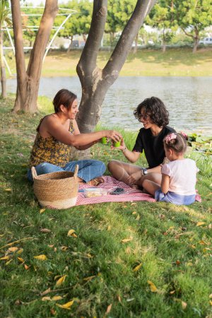 A family enjoys a tranquil afternoon picnic, engaging with each other by a calm lakeside.