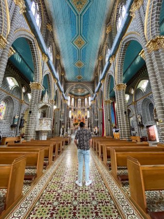A visitor stands inside a beautifully ornate church, admiring the intricate architecture, vibrant ceiling, and stained glass windows, captured from the aisle.