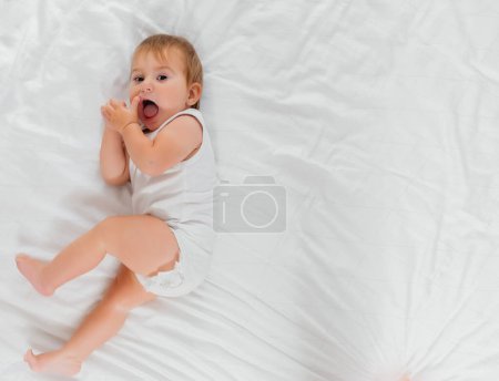 Téléchargez les photos : Un enfant sur un lit blanc le matin. Textiles et linge de lit pour enfants. Un nouveau-né s'est réveillé ou va se coucher. - en image libre de droit