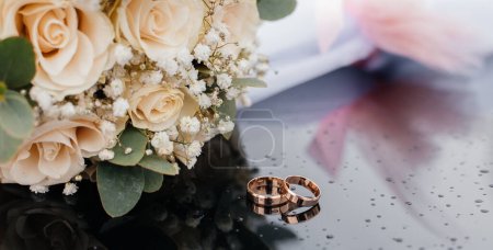 Photo for A beautiful toned picture with wedding rings lies on a black surface against the background of a bouquet of flowers. - Royalty Free Image