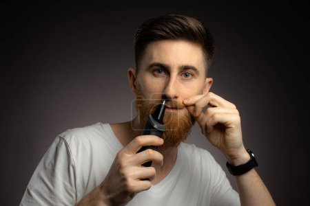 Photo for A young guy uses a nose trimmer to remove nose hair. - Royalty Free Image