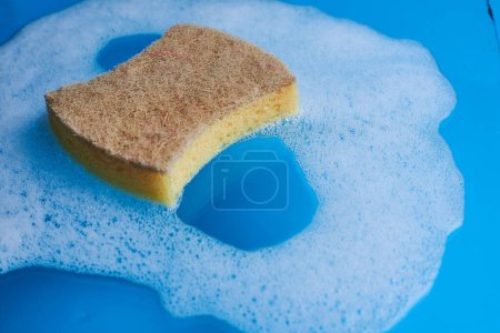 Photo for Yellow soapy sponge with foam on blue background. Cleaning concept. Copy space. - Royalty Free Image