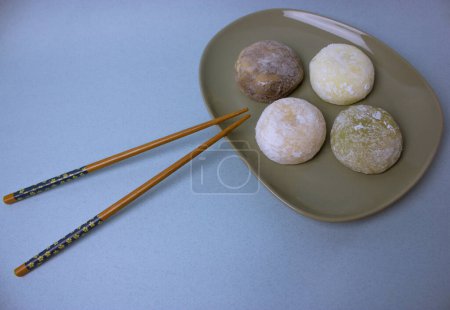 Baguettes et mochi dessert japonais traditionnel ou daifuku en pâte de riz close-up. Quatre boules de glace mochi sur plaque grise sur foyer sélectif de table bleu-violet. Asiatique sucré délicieux dessert.