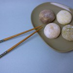 Chopsticks and traditional Japanese dessert mochi or daifuku in rice dough close-up. Four mochi ice cream balls on gray plate on blue-violet table selective focus. Asian sweet delicious food dessert.