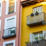 Yellow pink facades of residential apartment buildings houses in classical style. Balconies with plants, panoramic windows, doors with wooden shutters. European architecture details. Travel concept. 