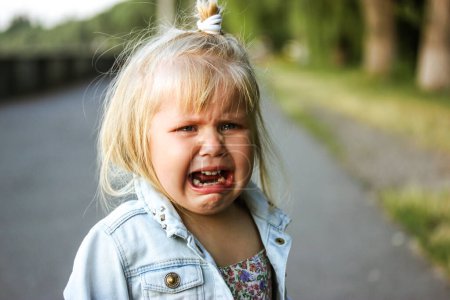 Photo for A little preschool-aged 3-5 year old girl is desperately crying loudly standing on a street. The child is lost. Negative emotions. White child refugee from Ukraine. Unhappy toddler kid from orphanage. - Royalty Free Image
