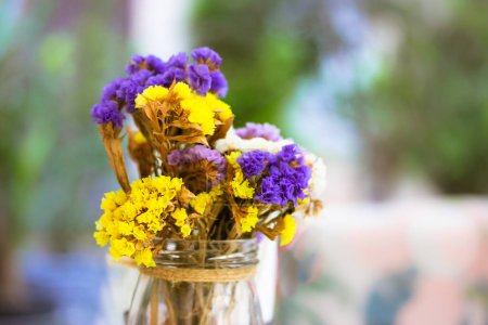 Ein Strauß farbenfroher getrockneter gelber, lila Statica Limonium Sinuat Blüten in einer Glasvase, Glas. Niedliche Blumenstillleben auf einem verschwommenen natürlichen Hintergrund im Sommer. Niedliche hübsche Blume Komposition. 
