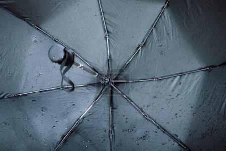 Téléchargez les photos : Parapluie humide noir, avec de petites gouttelettes d'eau de l'intérieur, rayons de parapluie. Mauvais temps, tempête d'automne ou de printemps. Accessoire pour la protection contre l'eau lors d'un jour de pluie - en image libre de droit