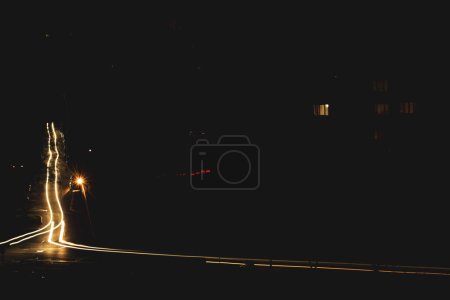 Foto de A dark city street at night and car headlights on a long exposure. A blackout in Kyiv due to the russian war in Ukraine. A global social problem with electricity. Darkness over town. Cars on roads. - Imagen libre de derechos