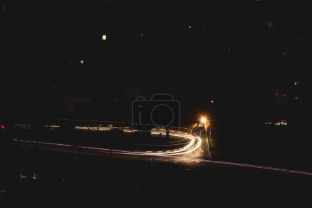 Foto de A dark city street at night and car headlights on a long exposure. A blackout in Kyiv due to the russian war in Ukraine. A global social problem with electricity. Darkness over town. Cars on roads. - Imagen libre de derechos