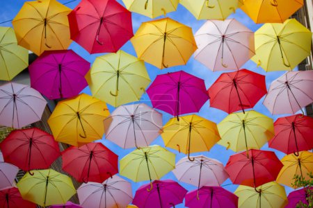 Téléchargez les photos : Background of lots of colorful brightly colored umbrellas in a blue sky view from below. Festive festival decorations of the city streets. Travel and leisure concept. Multicolor umbrellas hanging. - en image libre de droit
