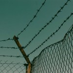 Barbed wire against a blue sky. Imprisonment, prison, unfreedom, repression concept. Private property, plant area protected by metal bars, fence, border Abstract background for a detective book cover.