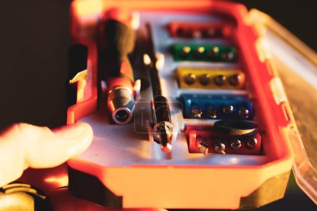 Ein Satz verschiedener Schraubendreher-Bits mit unterschiedlichen Befestigungen in einer orangefarbenen Plastikbox in einer Meisterhand. Verschiedene Schraubenzieher für Reparaturarbeiten. Werkzeugset für kleine Reparaturen. Schraubenzieher-Tip-Set.
