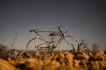 Téléchargez les photos : Un vélo miniature en métal contre un ciel bleu gris foncé. Jouet faux souvenir fabriqué à la main mini vélo artisanal dans une nature sauvage. Concept de VTT. La roue d'un vélo se tient sur une surface rocheuse. Journée mondiale du vélo. - en image libre de droit