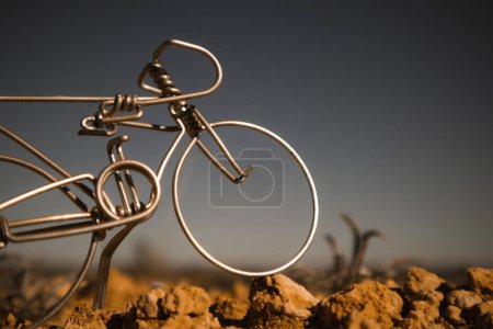 Téléchargez les photos : Un vélo miniature en métal contre un ciel bleu gris foncé. Jouet faux souvenir fabriqué à la main mini vélo artisanal dans une nature sauvage. Concept de VTT. La roue d'un vélo se tient sur une surface rocheuse. Journée mondiale du vélo. - en image libre de droit