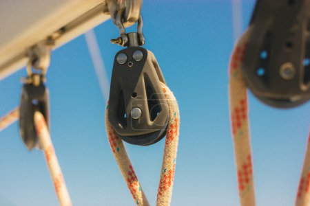Photo for Ship block with ropes. Steel sling and rope clamp connected by screw bolt. Device for adjusting the tension or length of ropes on the deck of a ship, yacht. Boat parts. Roller blocks against blue sky. - Royalty Free Image