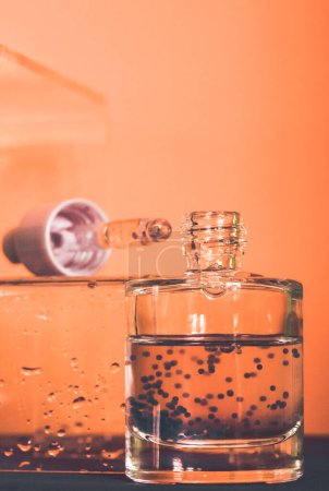 Hyaluronsäure in einer Glasflasche mit einer Pipette auf orangefarbenem Hintergrund gegen nasses Glas. Gesichtsserum oder Nagelhaut-Öl im Badezimmer. Hydro Boost Serum für feuchtigkeitsspendende alternde Haut. Ein Schönheitswerkzeug.