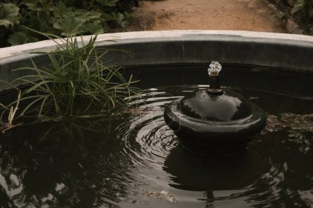 Téléchargez les photos : L'eau jaillit dans une fontaine décorative dans un parc, jardin. Détail ornemental d'une ancienne fontanette antique. Photo de la nature dans une touche sombre. Cercles sur l'eau noire. Concept de tranquillité, harmonie, zen. - en image libre de droit