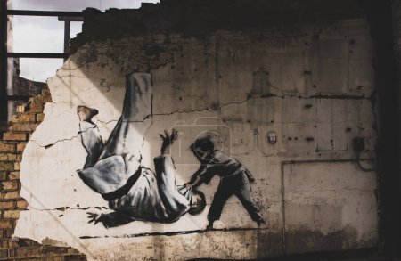 Téléchargez les photos : Borodyanka, Ukraine. 1er mai 2023 Graffiti peint par Banksy sur des bâtiments détruits. Garçon jetant l'homme en judo forme dessin sur le mur. Lieu du massacre de masse de civils par l'occupation des troupes russes en guerre. - en image libre de droit