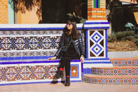 Photo for Madrid, Spain. February 13 2019 A young woman sitting on a decorated blue mosaic bench. A world solo traveler on vacation. Female travel blogger sits relaxed outdoors. Stylish girl on a city street. - Royalty Free Image