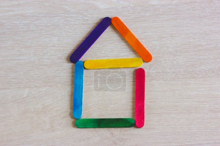 Symbolic toy house built from wooden colorful play sticks top view. Hometown real estate, home buying and renting concept. Bright colors house shape. Home made of wood ice lolly sticks on wooden table