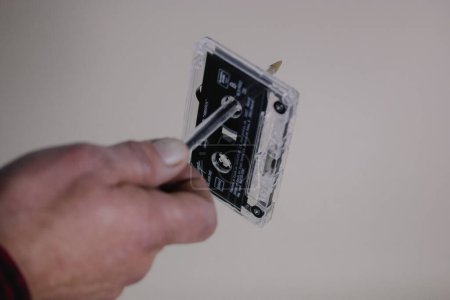 Foto de Madrid, España. Enero 2, 2024 El hombre está rebobinando con una pluma un viejo cassette vintage para el reproductor de grabadoras. Nostalgia de los 90, 00. Escuchar una música - Imagen libre de derechos