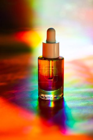 Glass cosmetic pipette bottle on multicolor rainbow light background. Decorative cosmetics on cosmetic table. Facial serum. Fashion magazine photo. 