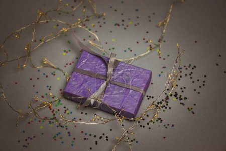 Beautifully wrapped in a violet box with a bow present among glowing LED garlands shining lights on blue background. Glowing illumination for New Year. Decor for celebration Christmas. Copy space.
