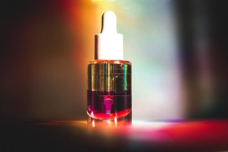 Glass cosmetic pipette bottle on multicolor rainbow light background. Decorative cosmetics on cosmetic table. Facial serum. No brand cosmetic product.