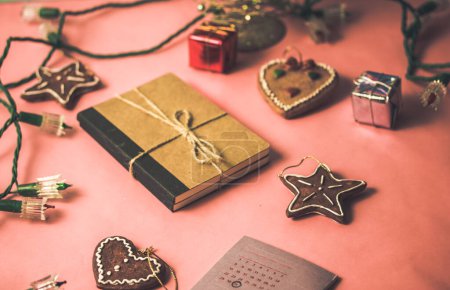 Composition esthétique des décorations et des cadeaux sur table rose. Un carnet kraft en papier brun se trouvait parmi les guirlandes, les jouets de Noël sous forme de biscuits en forme d'étoile, les guirlandes. Nouvel an décor festif pour la fête