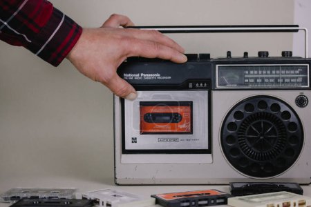 Photo for Madrid, Spain. May 2, 2023 A man put music cassette into an old record player. Nostalgia for '90s. Vintage tape recorder Ghetto blaster Music boom box - Royalty Free Image