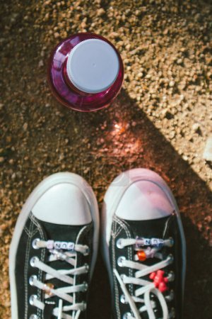 Foto de Madrid, España. enero 7, 2024 Negro vintage Converse zapatillas de deporte, pies de mujer, botella de color rosa con vista al agua. Zapatos vintage. Nostalgia de los 90. - Imagen libre de derechos