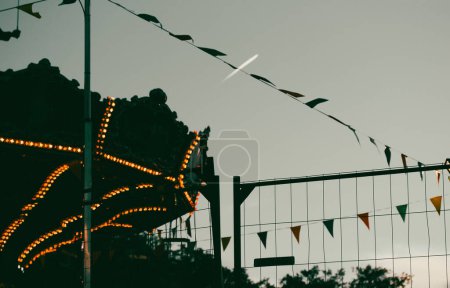 Photo for Carousel merry-go-round silhouette, triangles string garland against evening sky Fairyland, fairground background. Entertainments fun. Travel on plain - Royalty Free Image