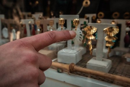 A woman chooses an expensive gold jewelry in a window of a jewelry store. Shopping, buying vintage jewelries. Finger points to earrings. Rich people.