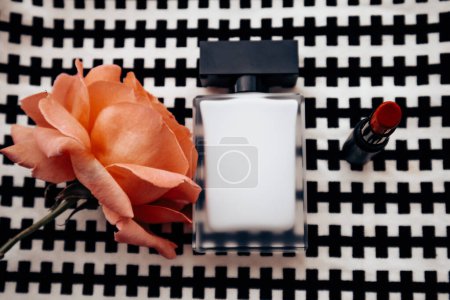 Botella de agua perfumada, lápiz labial rojo sobre fondo blanco negro, floreciente rosa de té fragante en la vista superior de la mesa. Concepto de belleza femenina. Estilo de vida femenino.