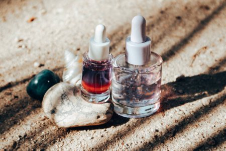 Anti-aging serum pipette bottles on a stone podium. Decorative cosmetics on a beige sand background with palm trees shadows. Female Skincare routine.