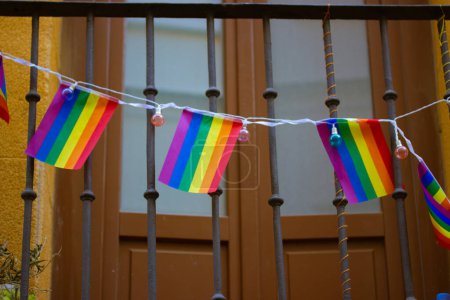 A balcony decorated with rainbow garland of LGBT flags. Cozy orange home. House exterior details. Pride month in Europe. Gay community neighborhood .