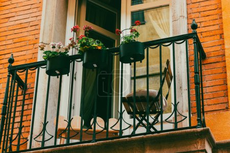 A balcony decorated with potted plants and blooming flowers. Plant-pots for home exterior decor. Place for relax, lounge space outdoors of red house. 