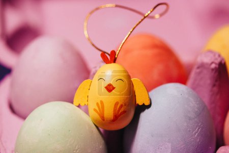 Painted Easter eggs on pale pink background. Bright yellow funny jolly toy chicken amongst painted Easter eggs. Decor for traditional spring holiday.