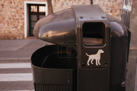 A black urn with an image of a dog on a city street. A concept of a lifestyle of dog owners. Waste bin outdoors. Urban lifestyle. Environment issue.