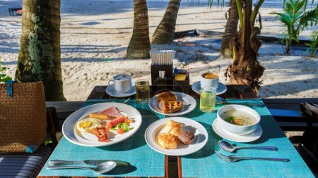Téléchargez les photos : Petit déjeuner sur une plage tropicale en Thaïlande. fruits, café, soupe de riz thaïlandais et pain - en image libre de droit