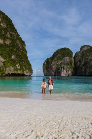 Foto de Pareja caminando en una playa vacía, las mujeres tailandesas y los hombres caucásicos caminan en la playa de Maya Bay Koh Phi Phi Tailandia por la mañana con turqouse color océano. - Imagen libre de derechos