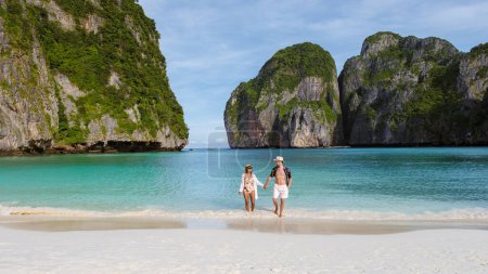 Foto de Las mujeres tailandesas en trajes malos y los hombres caucásicos en nadar paseos cortos en la playa de Maya Bay, playa Koh Phi Phi Tailandia por la mañana con turqouse color océano. - Imagen libre de derechos