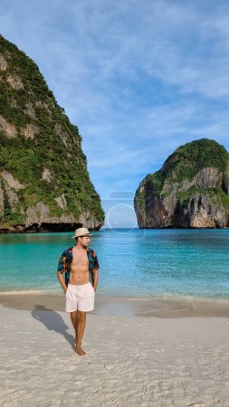 Photo for Young sun tanning men with swim shorts and a hat on the beach of Maya Bay Koh Phi Phi Thailand. - Royalty Free Image