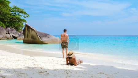 Téléchargez les photos : Un couple d'hommes et de femmes se détendre bronzant sur la plage de sable blanc tropical avec turqouse couleur océan des îles Similan Thaïlande. - en image libre de droit