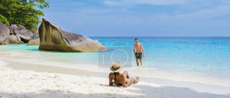 Téléchargez les photos : Un couple d'hommes et de femmes se détendre bronzant sur la plage de sable blanc tropical avec turqouse couleur océan des îles Similan Thaïlande. - en image libre de droit