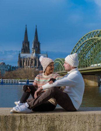 Téléchargez les photos : Un couple en voyage à Cologne Allemagne pendant l'hiver en Europe assis au bord du Rhin regardant le Dom de Cologne - en image libre de droit