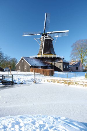 Foto de Molino de viento de madera en la nieve en los Países Bajos durante el invierno. Clima frío en Holanda con nieve y molino de viento - Imagen libre de derechos