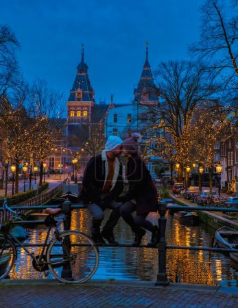 Téléchargez les photos : Un couple en voyage à Amsterdam avec des lumières de Noël aux canaux pendant l'hiver aux Pays-Bas - en image libre de droit